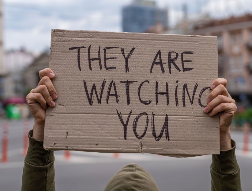 person holding up sign with text 'they are watching you'